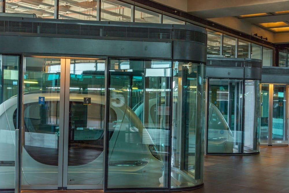 A series of modern, glass-enclosed automatic doors, possibly at an airport or large facility, with reflections of the interior space.